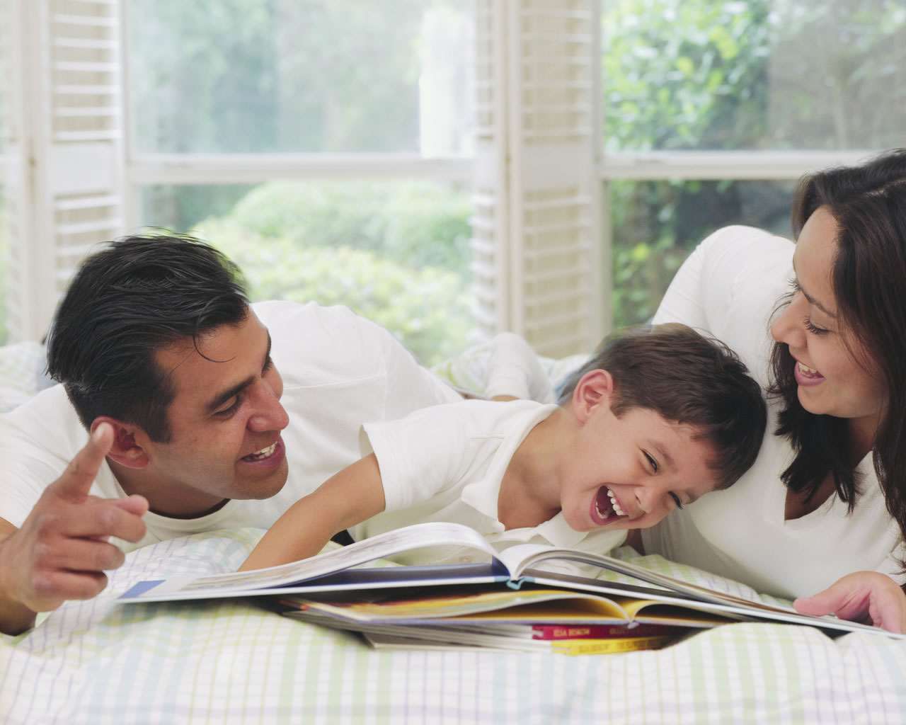 Small child laughing and reading with two parents